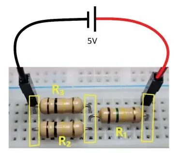 A foto a seguir mostra um circuito com três resistores (𝑅1, 𝑅2 e 𝑅3) conectados em uma protoboard (base de contatos)